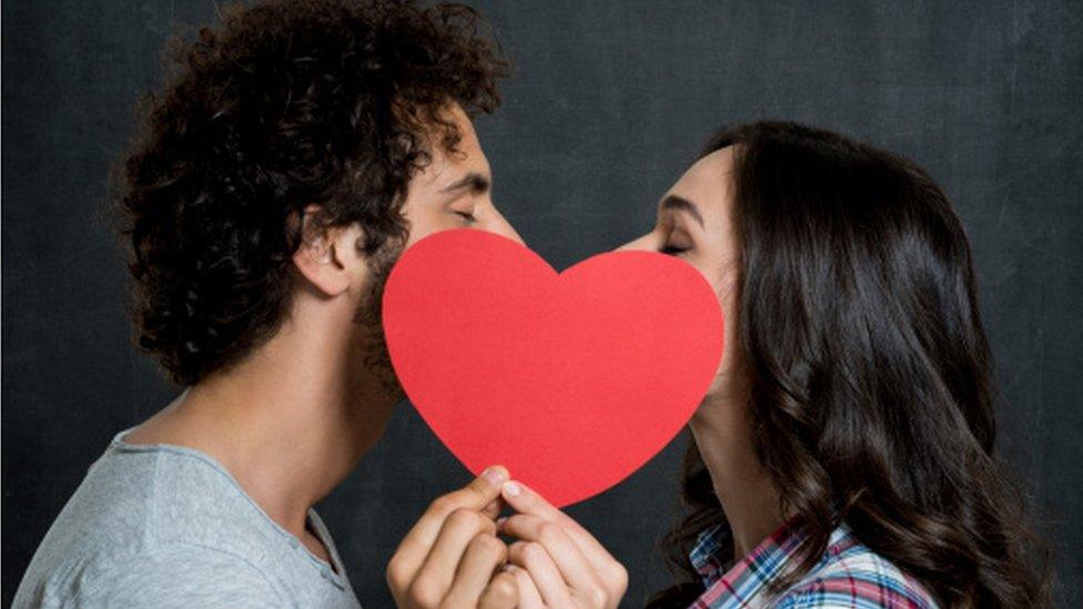 Two lovers kissing behind a heart