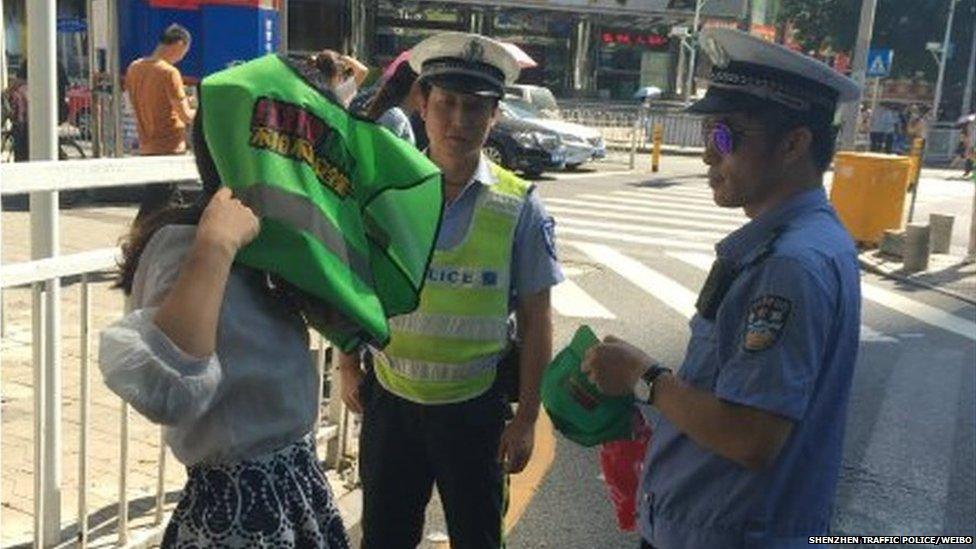 A woman being made to put on a green vest by a police officer