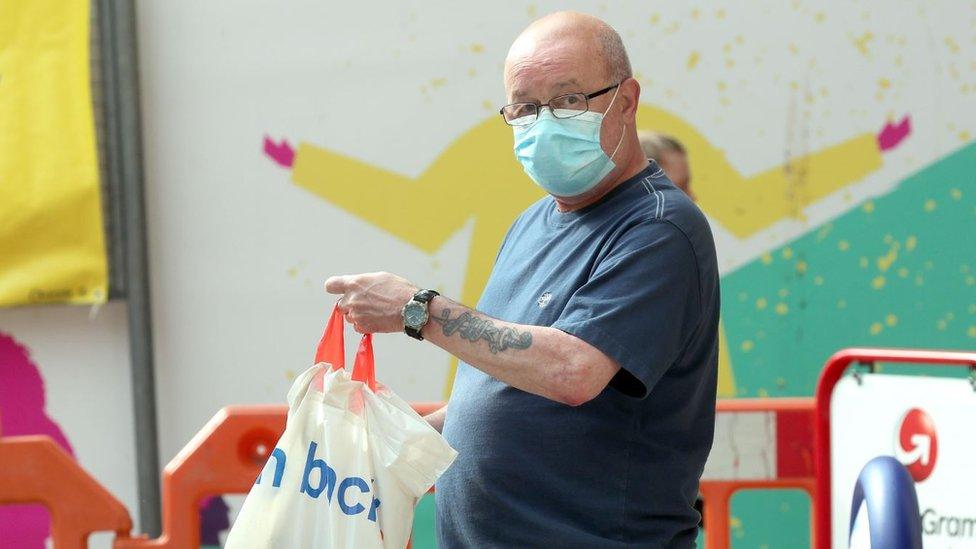 A shopper holding a Tesco bag and wearing a face covering