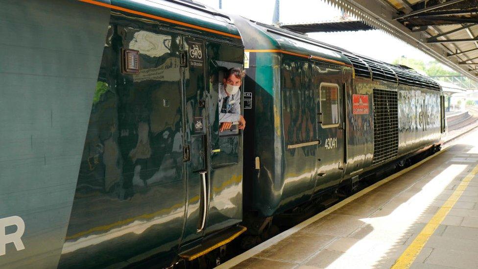 A Great Western Railway driver wearing a mask leans out of a train