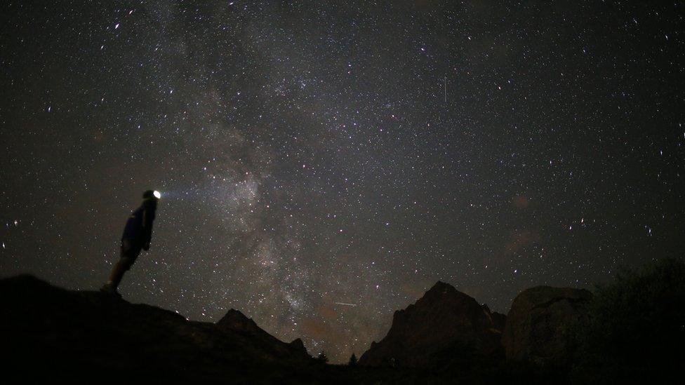 A hiker gazes up at the night sky which is full of stars and meteors