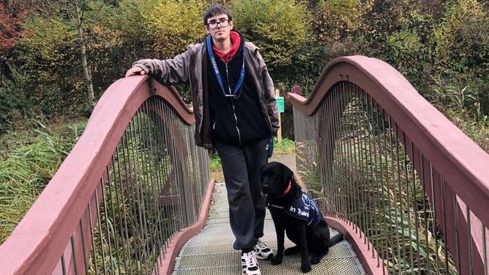 Jake Baker on a footbridge with a black service dog