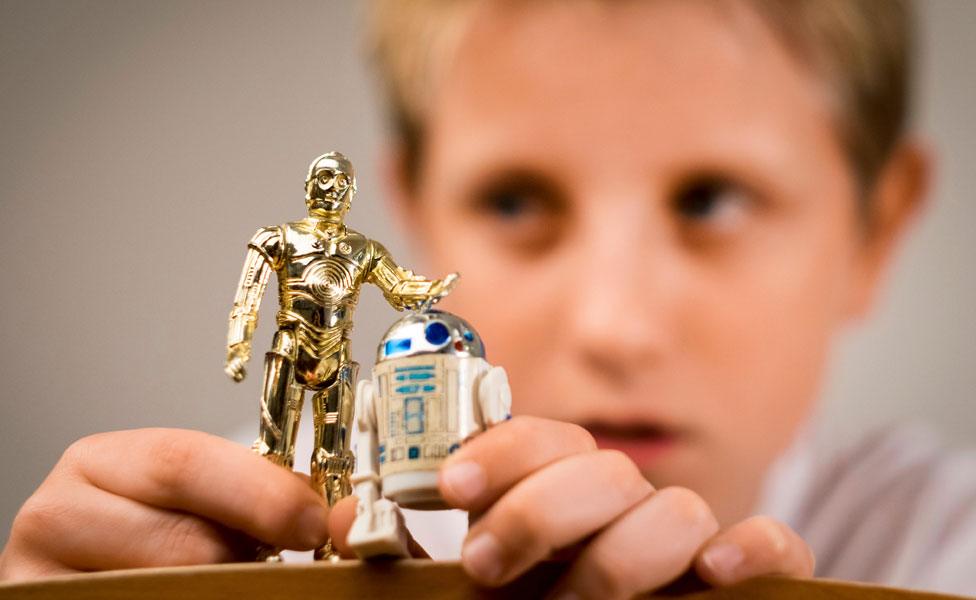 A boy playing with two Star Wars figures