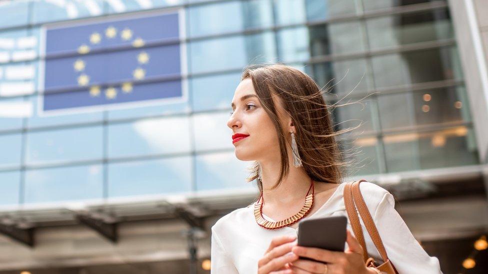 Young woman holding phone standing near EU flag