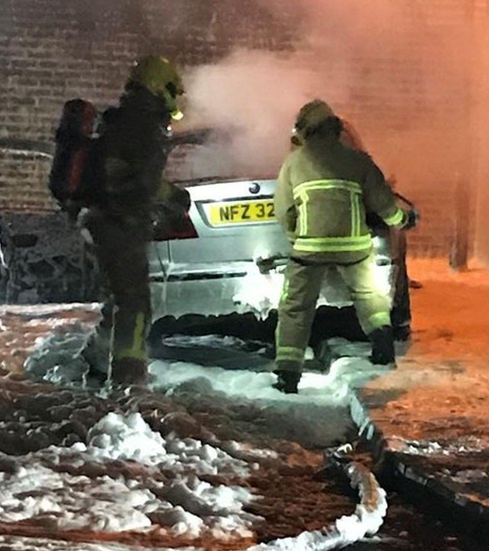 Firefighters deal with the burnt out silver Saab