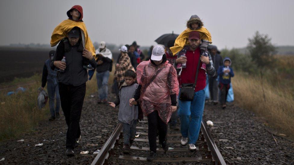 Syrian refugees walk along a train track