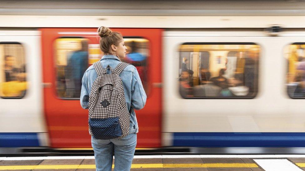 woman standing waiting on a train platform as a train moves into the station