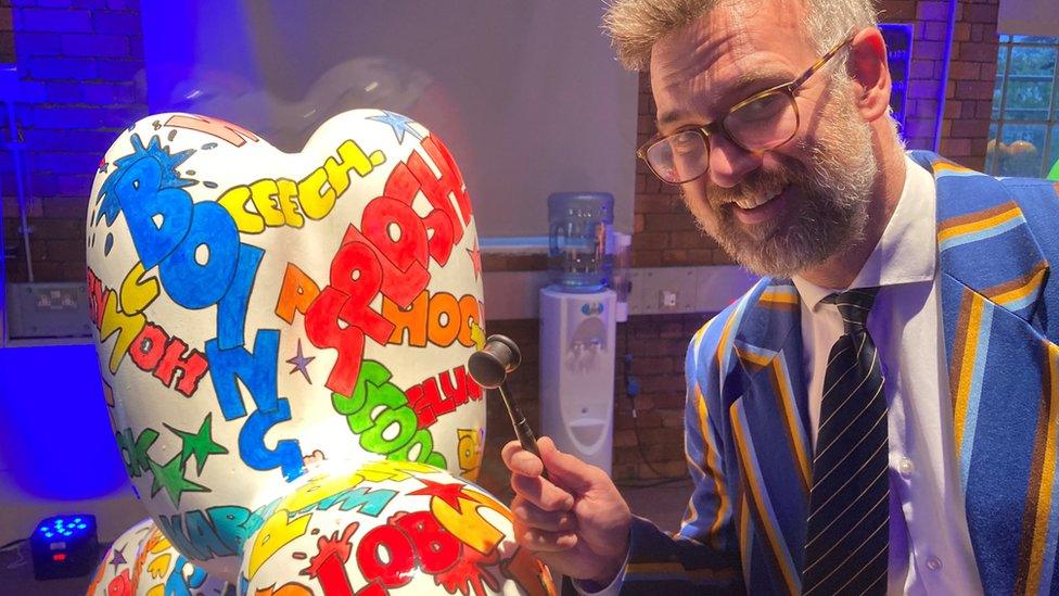 Auctioneer Charles Hanson with his gavel next to a colourful cartoon Swindog