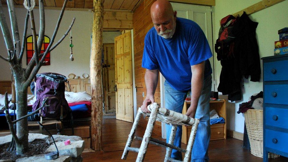 Andy places down a hand-thatched stool by a tree in the centre of a room.