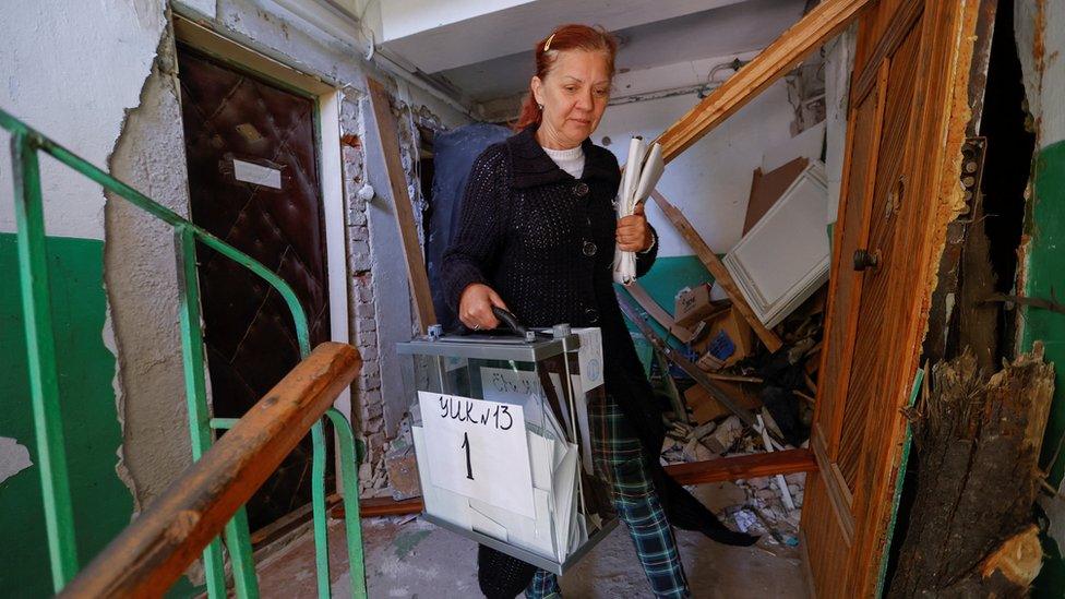 An electoral worker carries a ballot box through a ruined block of flats in Mariupol, 25 September