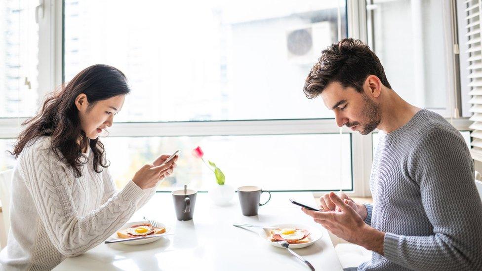 Couple drink tea as they look at their phones