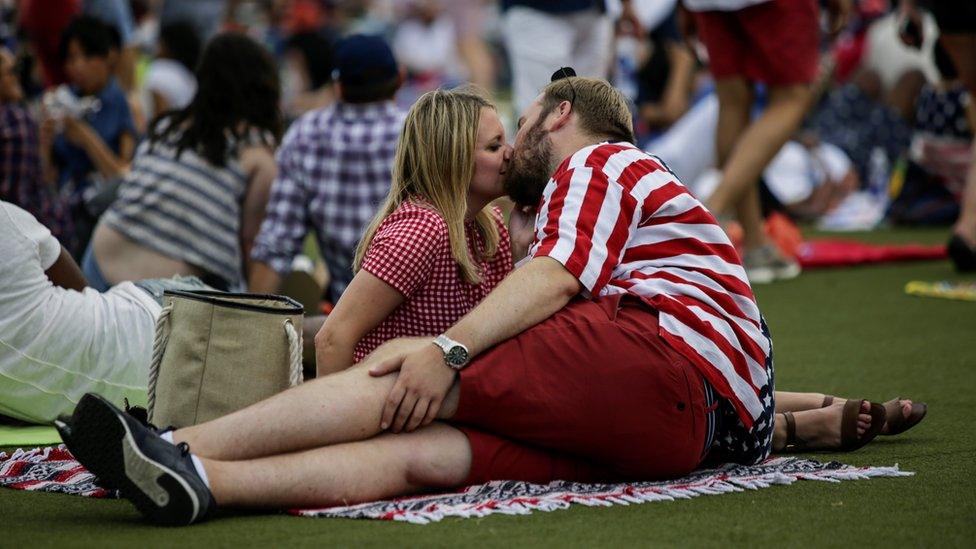 A couple, dressed in US flag colours, kiss on a blanket on the grass