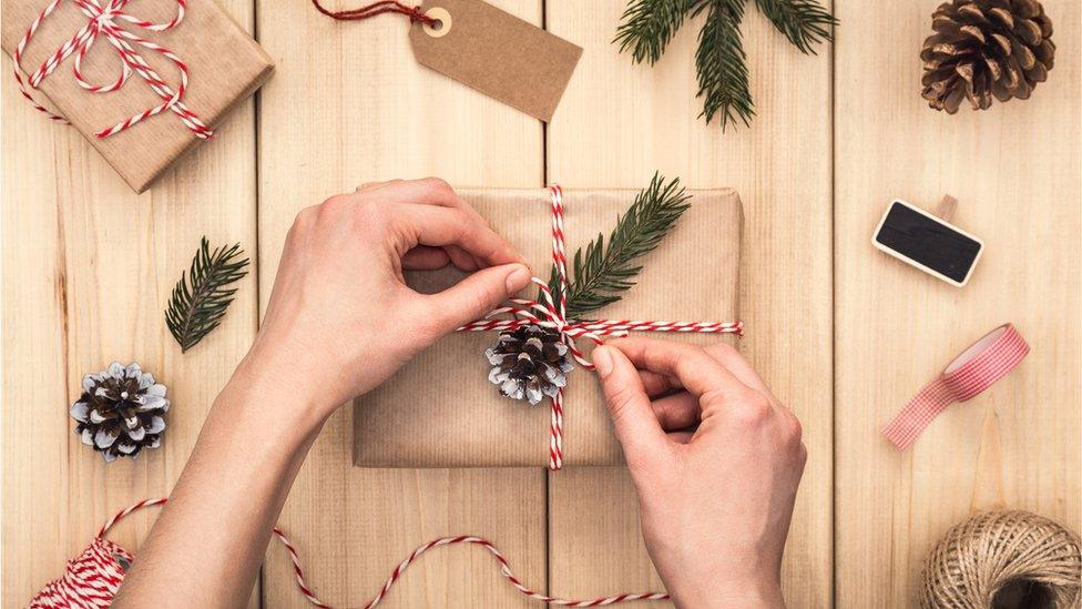 Hands wrapping a gift over wooden table. Top view of Woman preparing present. Directly above. Christmas time.