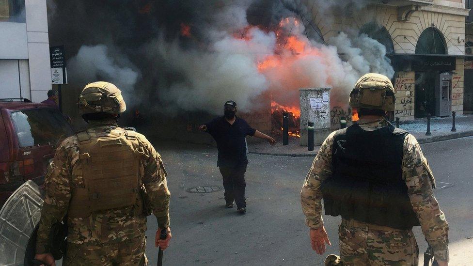 A man gestures to soldiers in front of a bank set on fire by protesters in Tripoli, Lebanon (28 April 2020)