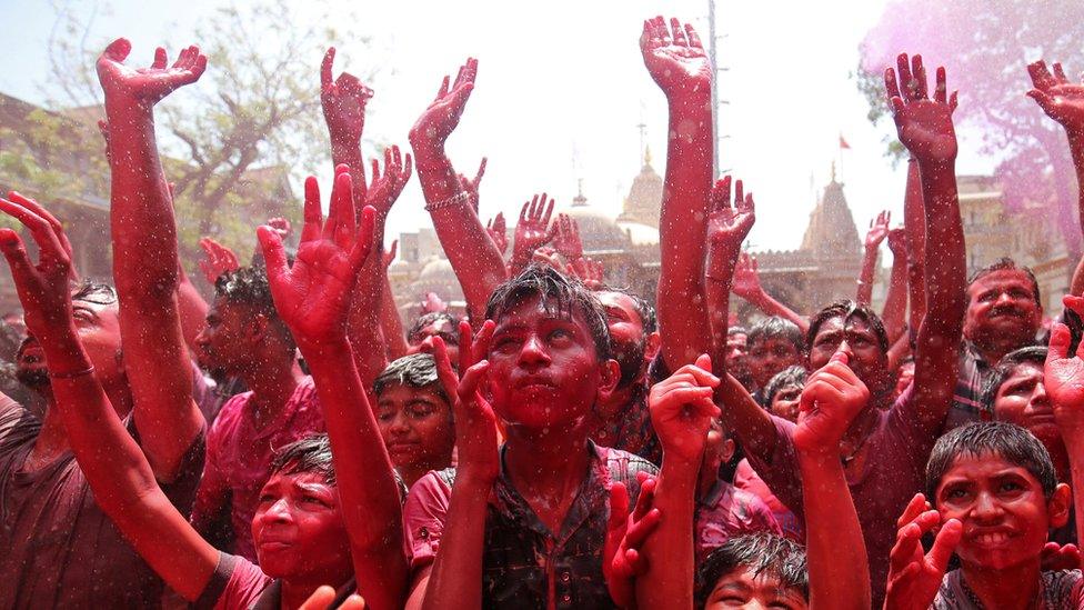 A crowd completely covered in colours hold their hands in the air