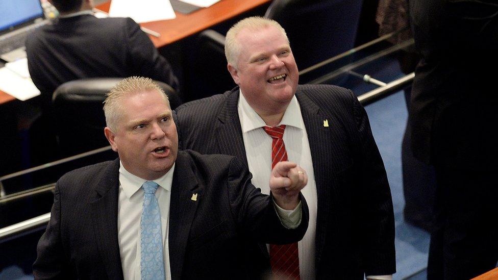 Doug Ford (L) reacts to someone in the city council chambers while Rob Ford looks on