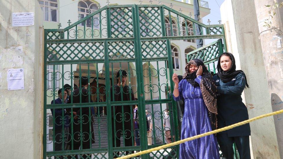 women leaving a building, one being comforted by the other