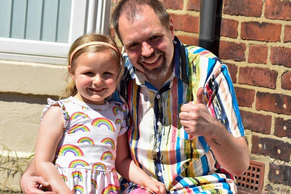 A young girl with her father who is giving a "thumbs up" sign