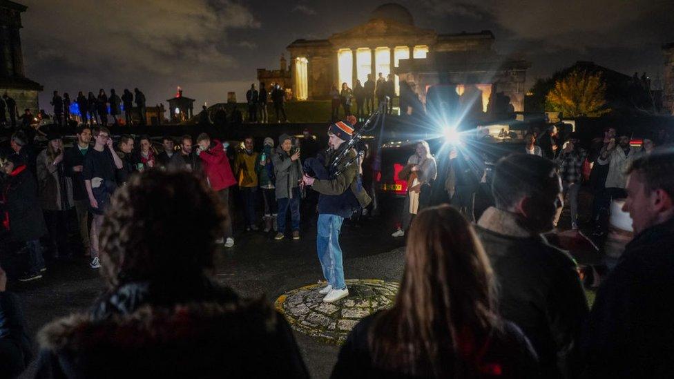 A bagpiper plays in front of a crowd at Calton Hill in Edinburgh