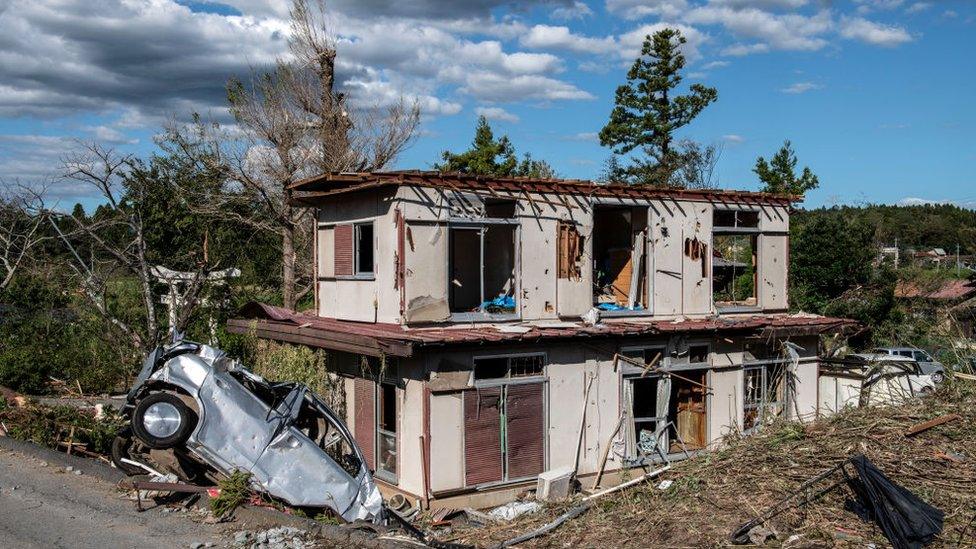 An upturned car lies next to a partially destroyed house after being hit by a tornado shortly before the arrival of Typhoon Hagibis