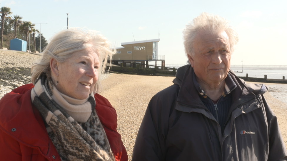 Terri Stanley wearing a red coat and Eric Stanley in a black coat on the beach in Southend