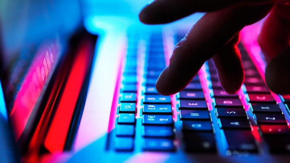 A hand over a laptop keyboard, which is illuminated in red