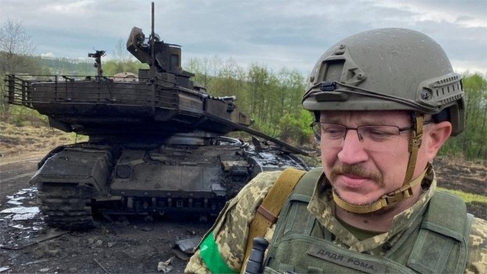 A Ukrainian soldier stands next to a destroyed Russian tank