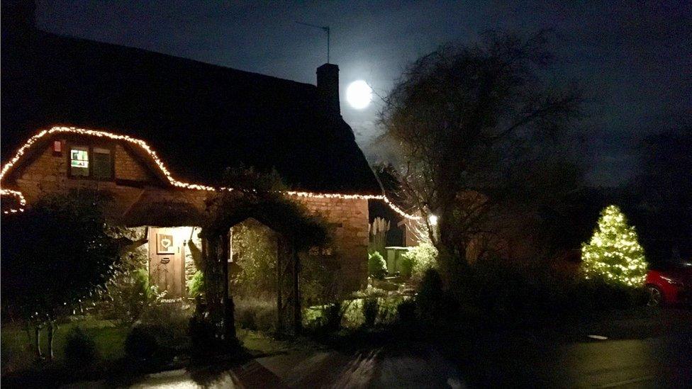 The supermoon between a house and tree appearing to be close to the ground