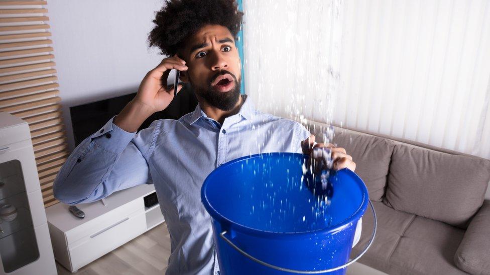 A man holds a bucket under a leaking pipe