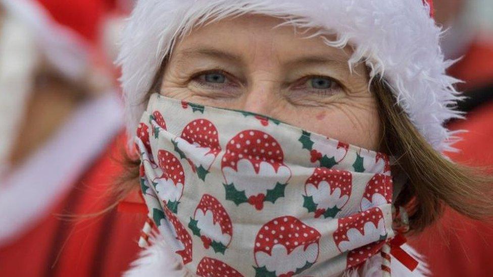 Woman dressed as Santa in a mask with Christmas puddings on it