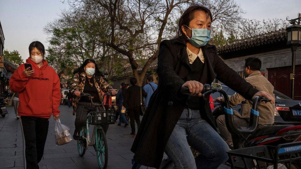 Women wear protective masks as they walk and ride shared bikes in Beijing.