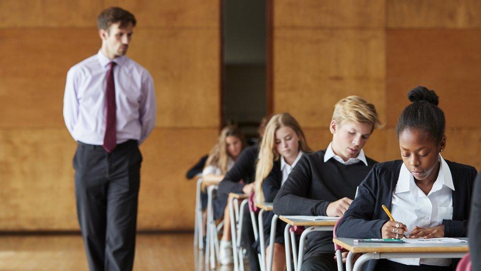 A row of pupils taking exams and a teacher invigilating