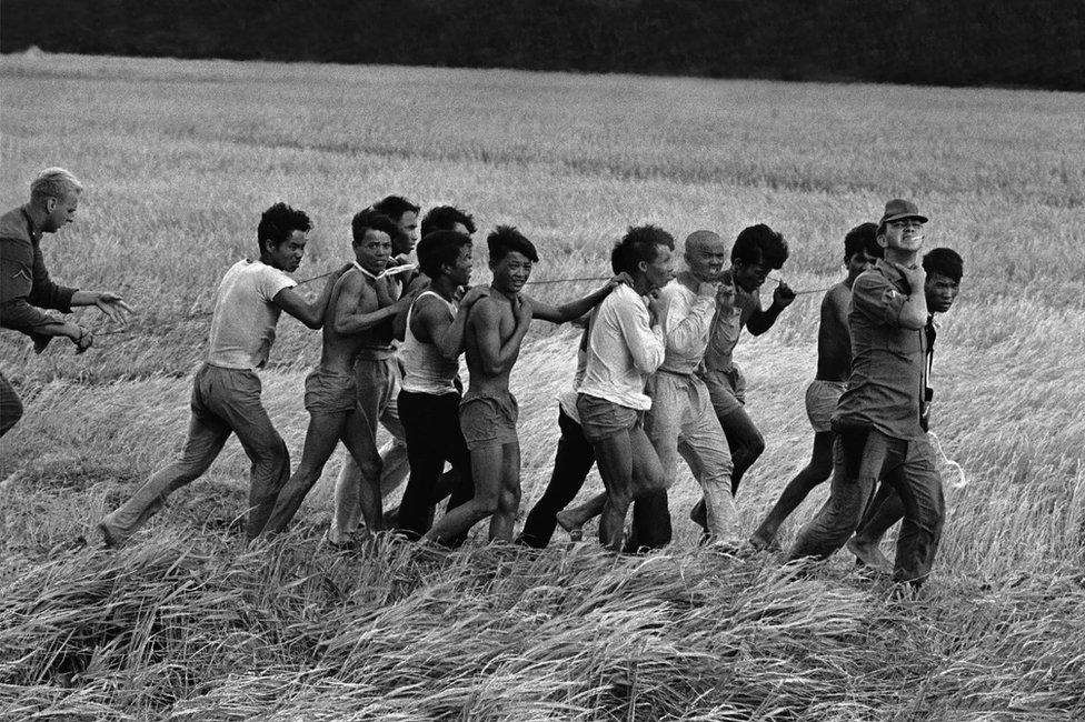 A group of tied Vietnamese soldiers are led across a field