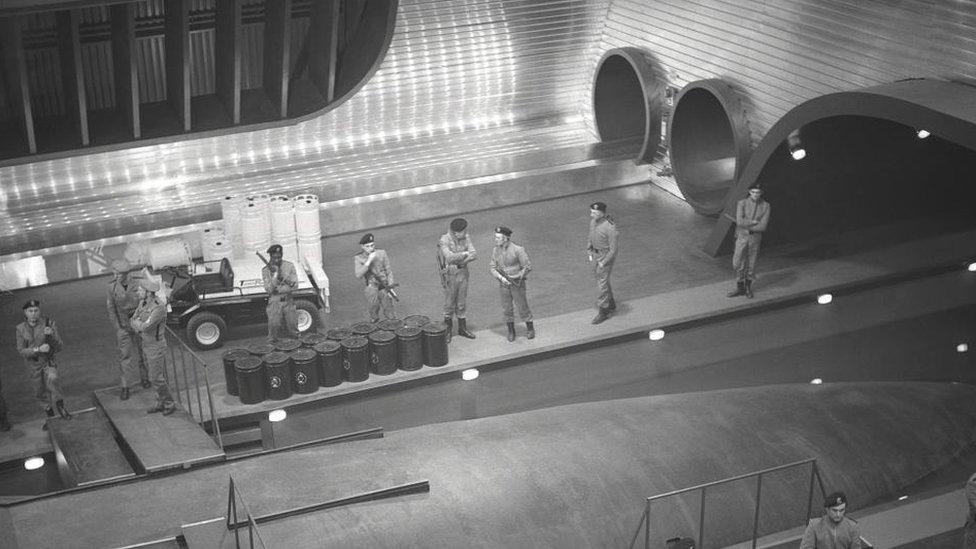 Large film set showing submarines and military personnel standing to attention