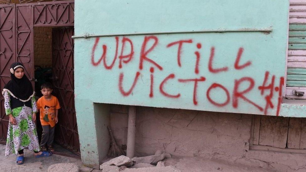 Indian Kashmiri children stand next to graffiti that reads "War till Victory" during a curfew in Srinagar (08 July 2017)