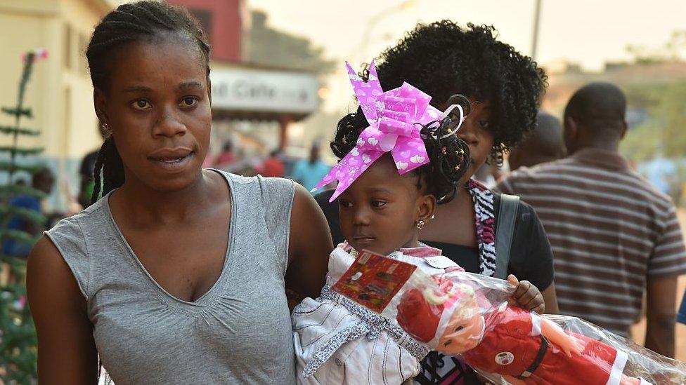 A mother carries her daughter after shopping at the local market for Christmas goods in Bangui, 2015