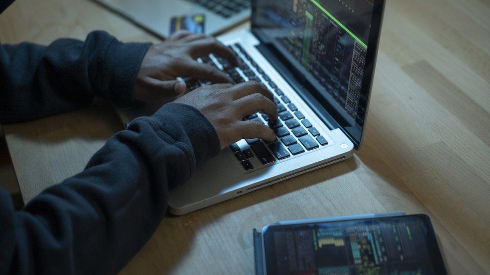 A hacker working on a computer, while monitoring data on a tablet