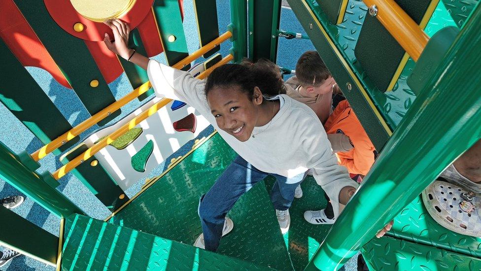 Mia and another child inside the frame walk up the steps to the slide