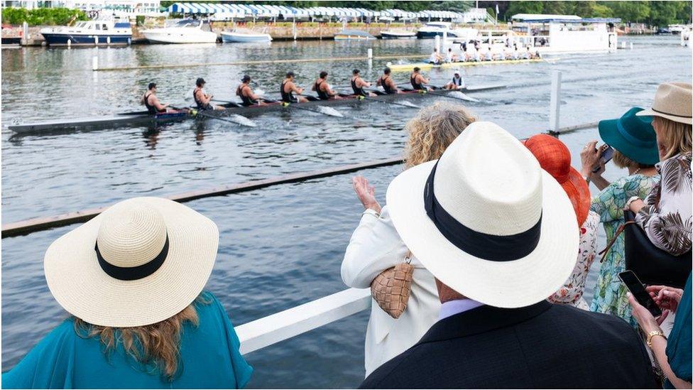 People watch rowers on the river