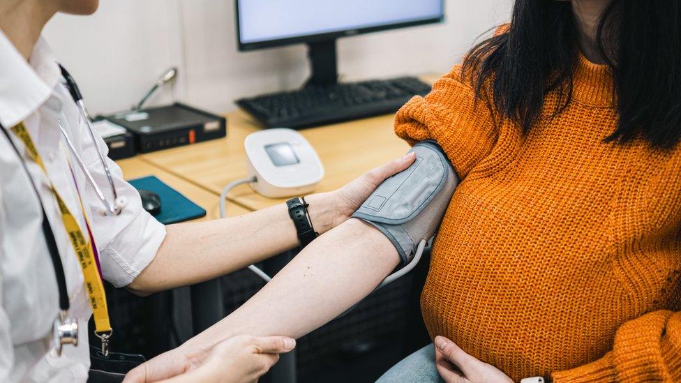 Pregnant woman wearing a baggy jumper has her blood pressure taken by doctor