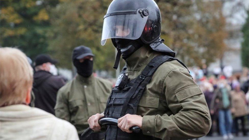 Law enforcement officer in black helmet and holding truncheon at a rally in Minsk (12 October)