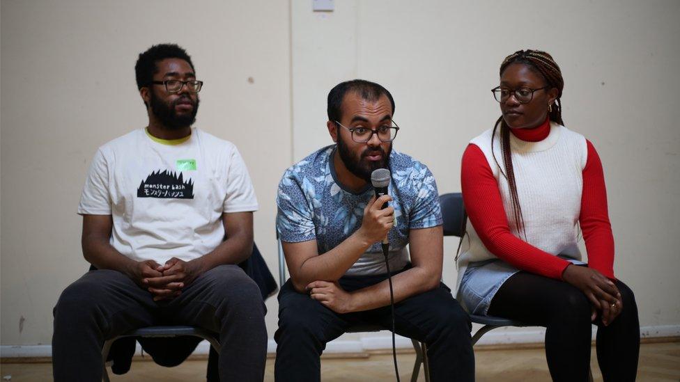 Three young people who work with Babbasa sat in a row on chairs the middle person wearing glasses is peaking into a microphone