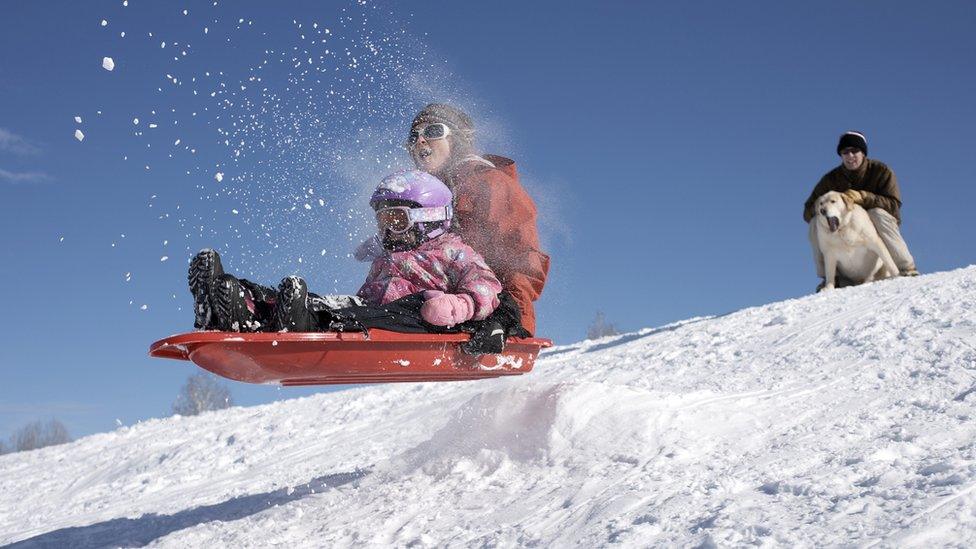 mum and daughter do a jump on a sledge in the snow - a dog is barking at them