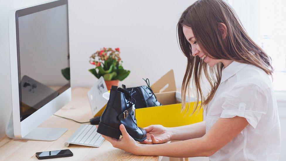 A woman opens a box containing new shoes at her desk