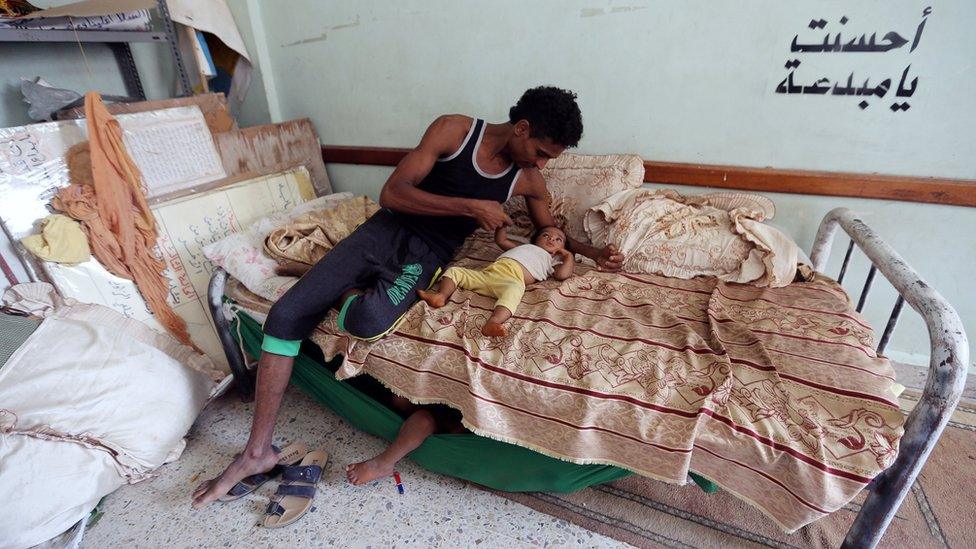 A man sits on a bed with a child at a school housing displaced people near Hudaydah airport (18 June 2018)