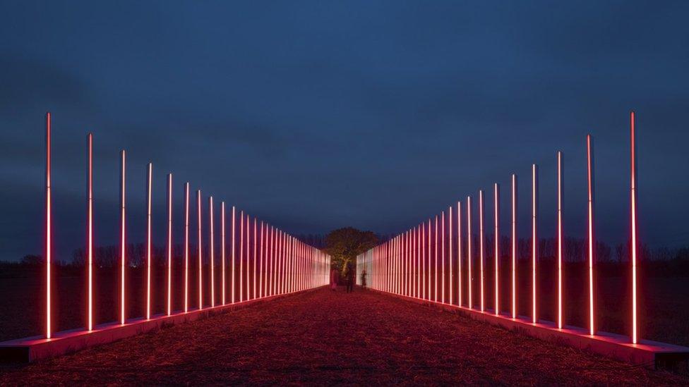 A long line of red vertical lights span across a field