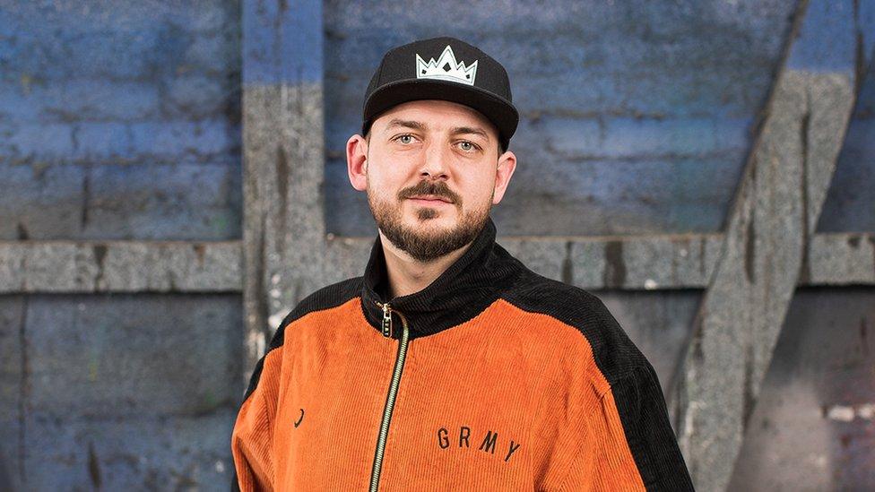 Jesse Jones with short brown beard wearing black cap and orange top backstage at a theatre