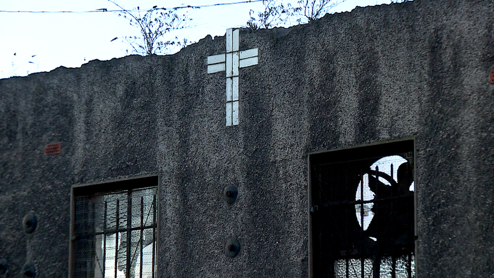 Rear of a derelict building, a cross formed in tiles on the wall