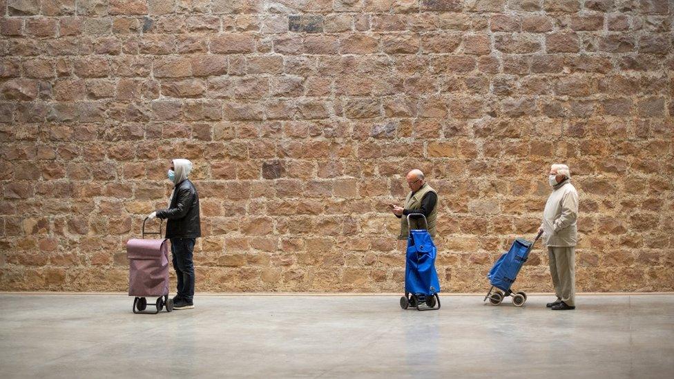 People keep their distance as they wait their turn in a queue to access a Lidl supermarket in Barcelona