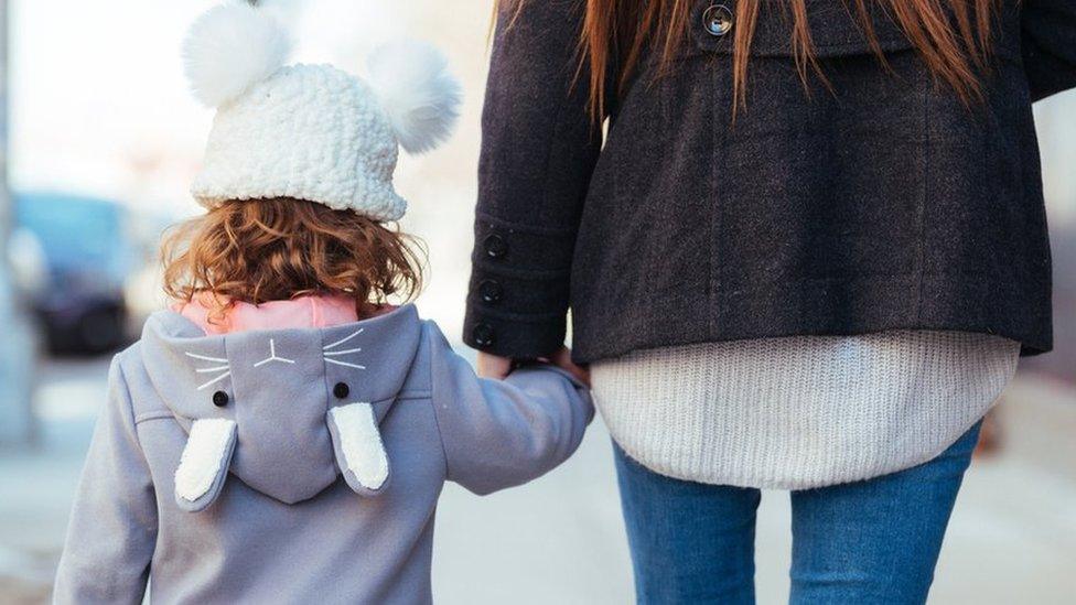 A woman holds her daughter's hand